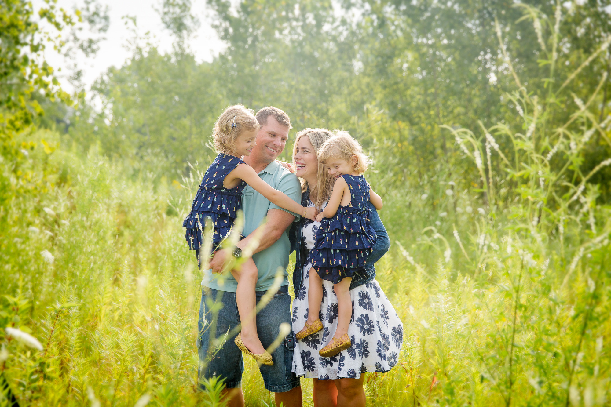 family laughing and interacting with mom and dad holding daughters standing in nature
