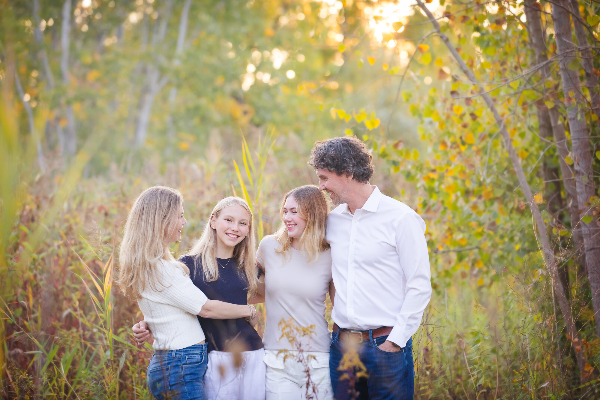 family with two teenage daughters hugging and laughing in a field with beautiful light