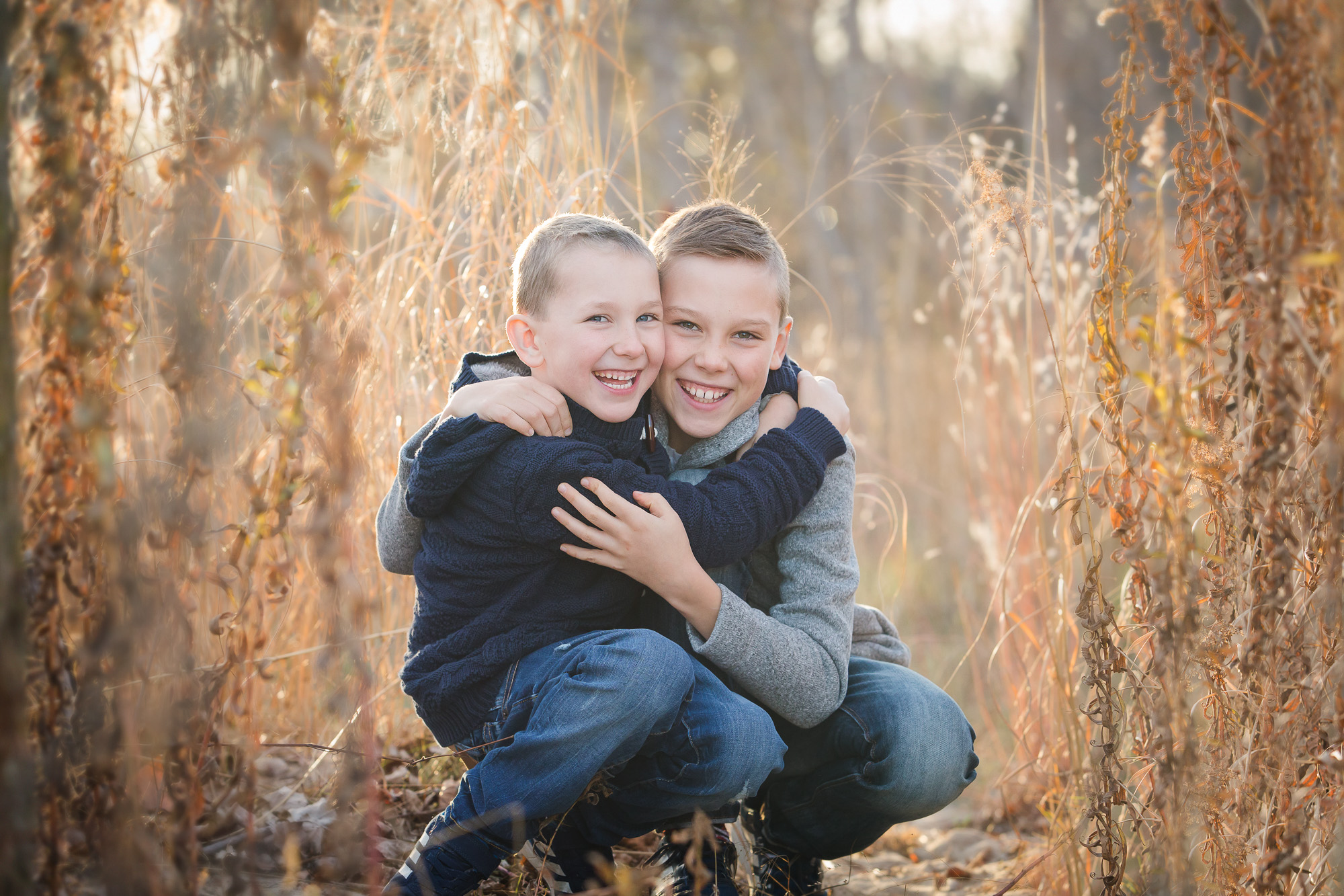 two preteen brothers hugging and laughing in a fall scene with golden tones