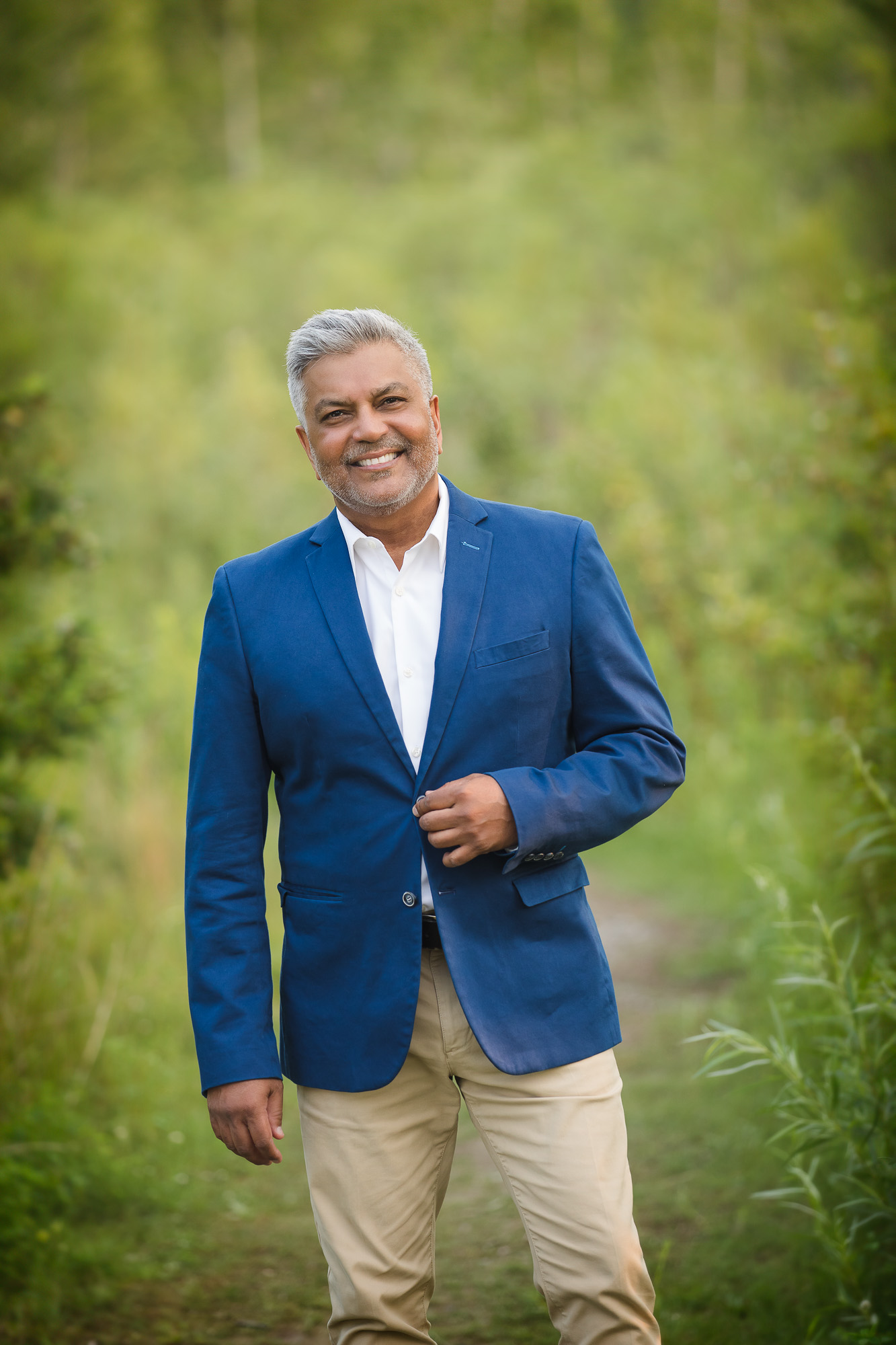 well dressed south asian man standing in field with his hand on his jacket button